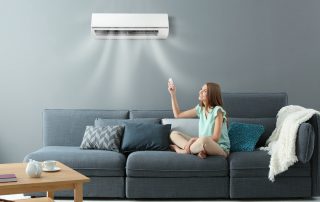 Young woman switching on air conditioner while sitting on sofa at home