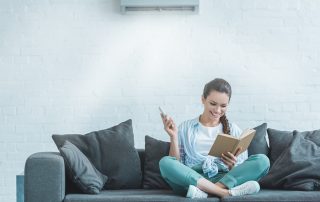 Happy woman reading book while turning on air conditioner with remote control at home