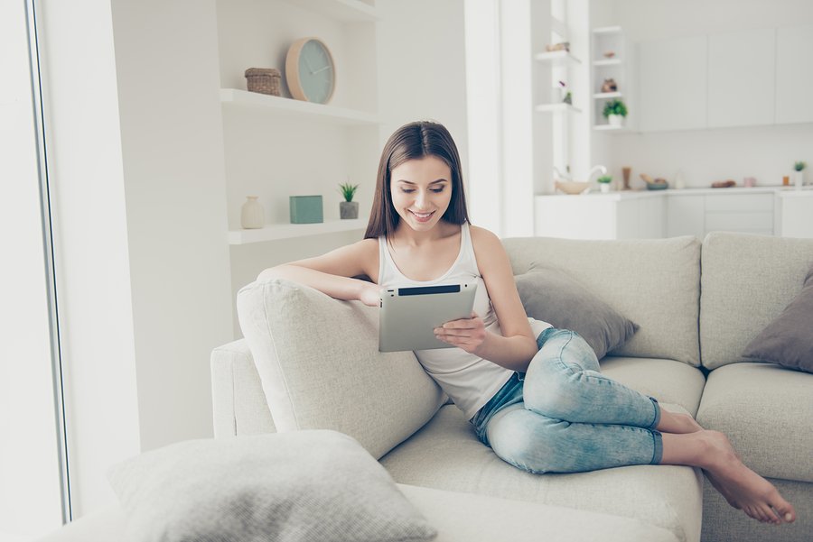 Full legs body size sweet gorgeous nice adorable good-looking lady with her brunette hair beaming toothy smile she sit indoor cosy modern apartment room in denim jeans look at tablet